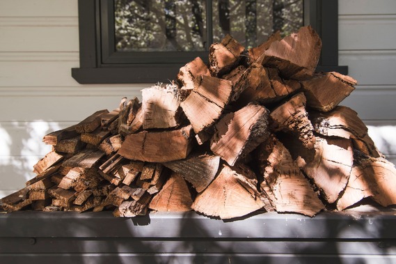 A stack of chopped wood pieces piled in front of a window on an outdoor surface.